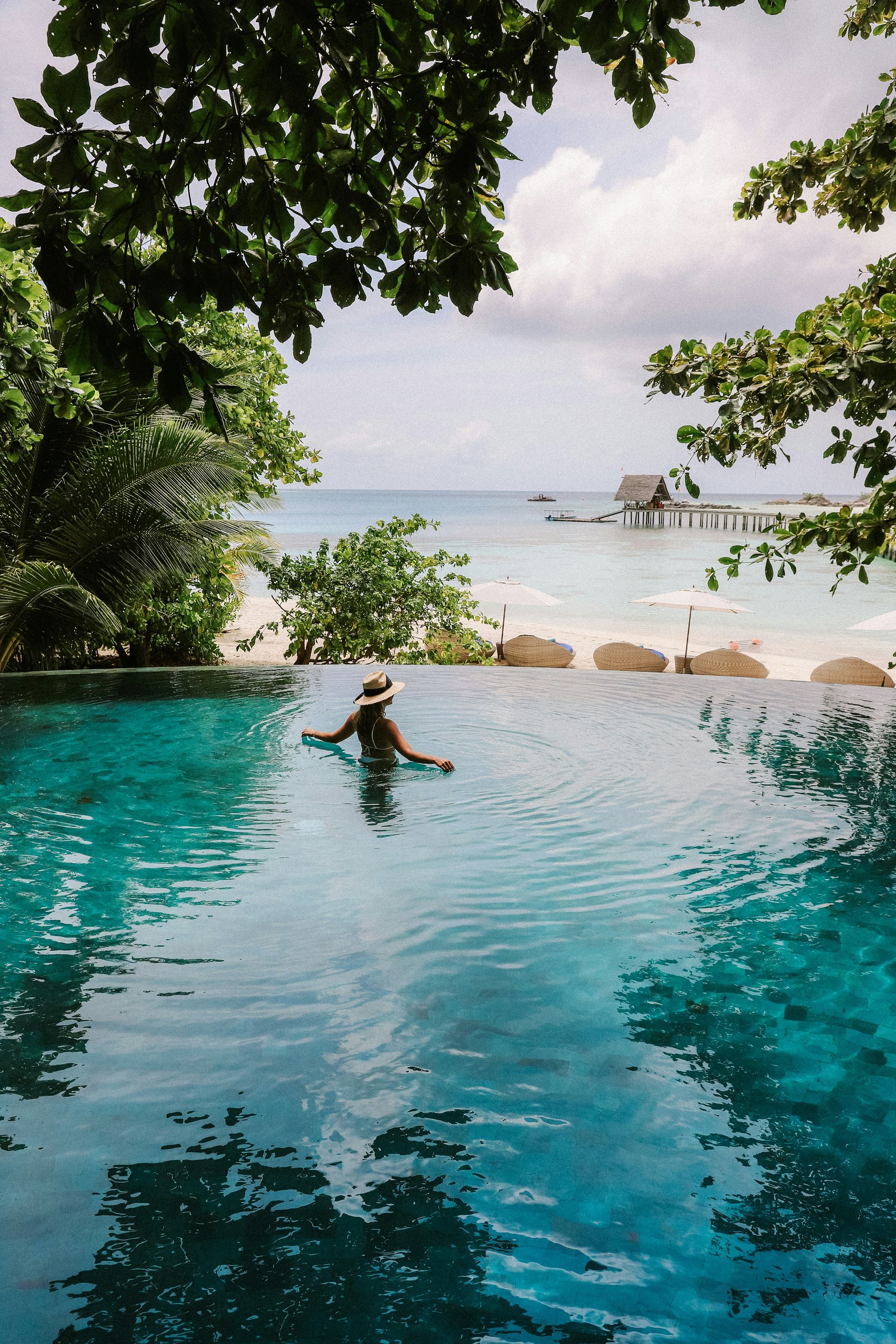 awoman in an infinity pool at a tropical location.  She is looking out to sea.